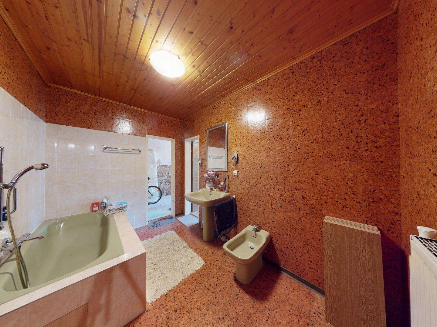 Badezimmer mit Badewanne, Waschbecken und Bidet, gekennzeichnet durch eine Holzdecke und auffällige Wandverkleidung.