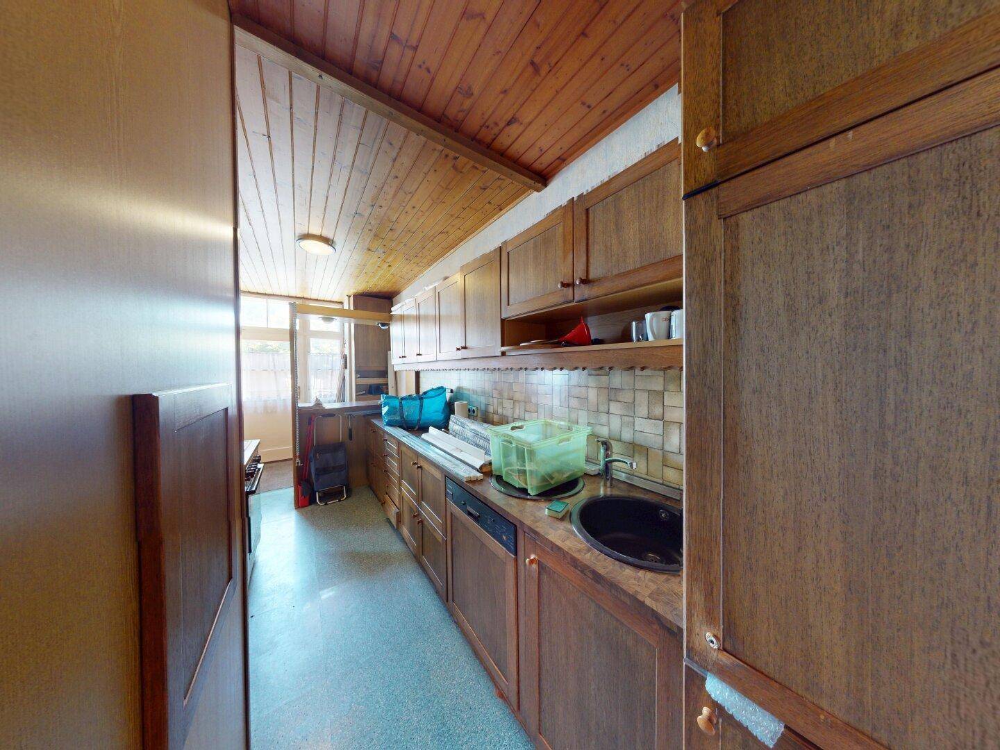Küche mit Holzschränken, schwarzem Spülbecken und einem Fenster, ergänzt durch eine Holzdecke.