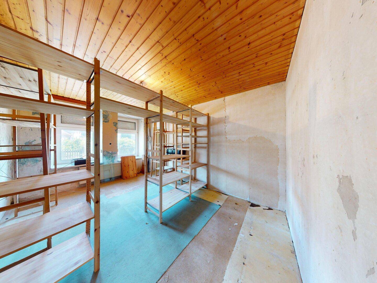 Weiterer Blick in den Abstellraum mit Holzregalen, Holzdecke und unfertigen Wänden.
