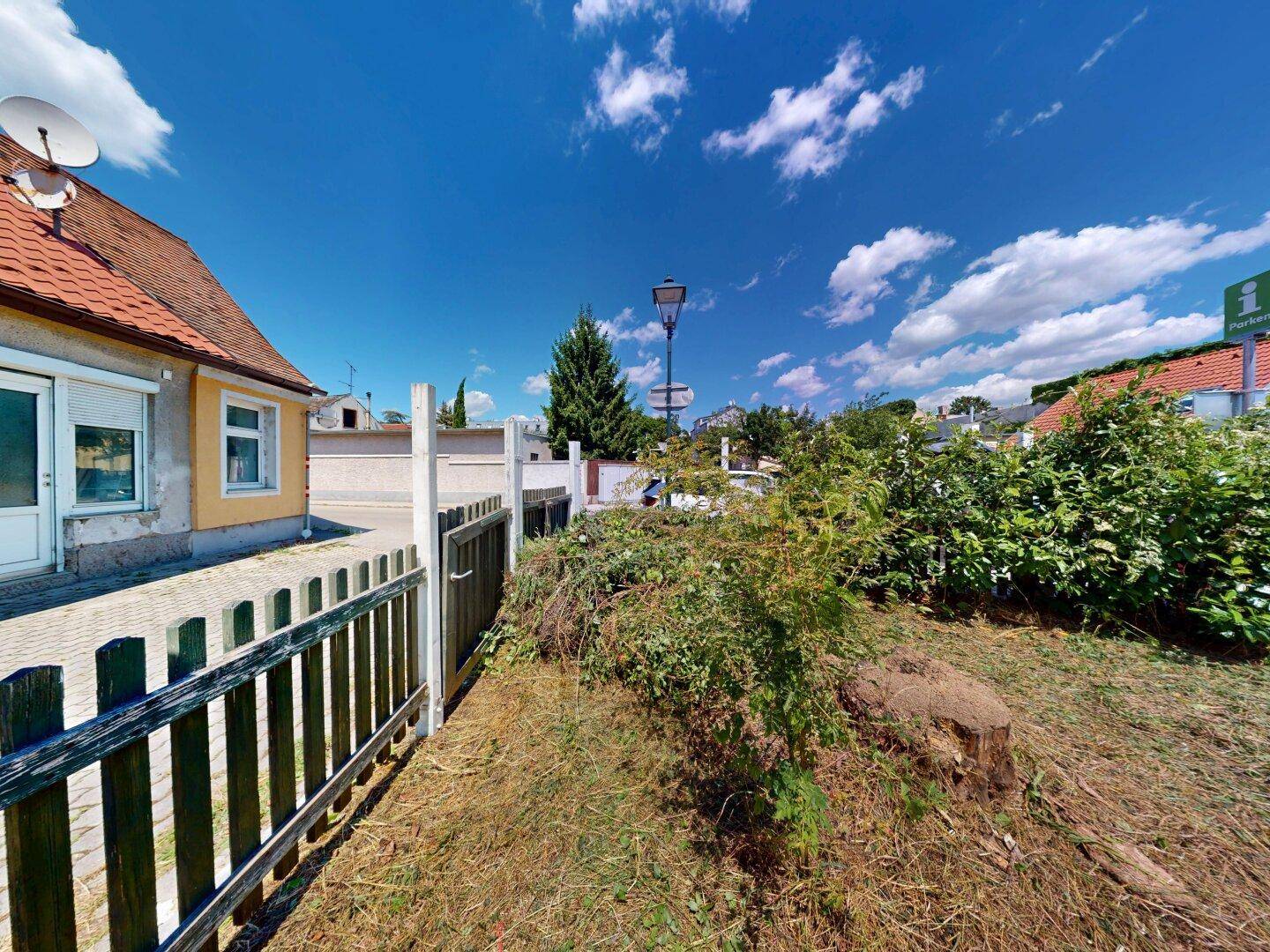 Außenbereich mit Holzzaun und einem verwilderten Garten, der das Haus umgibt.