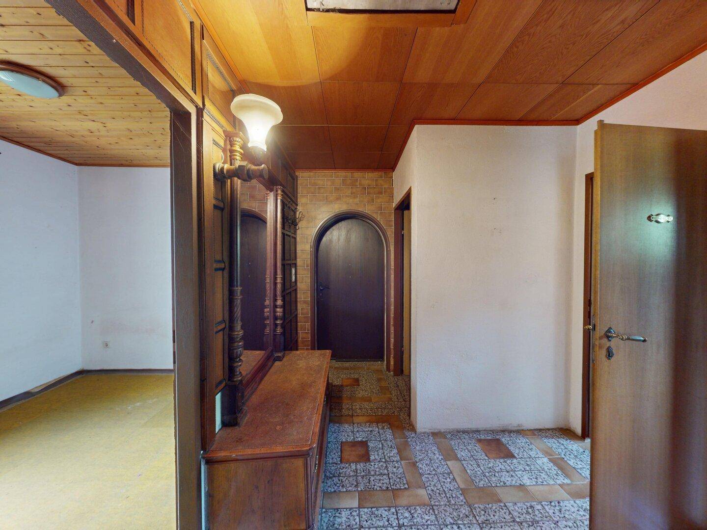 Traditioneller Flur mit Holztäfelung an der Decke, gemusterten Fliesen und einem antiken Spiegelschrank.