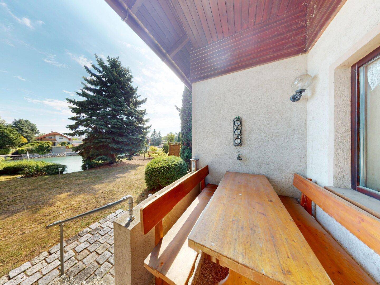 Überdachte Terrasse mit rustikalen Holzmöbeln und einem schönen Blick auf den Garten und den See.