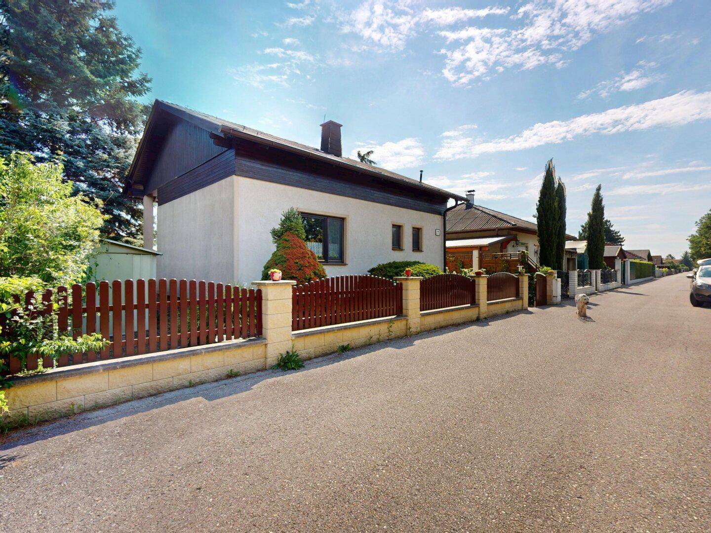 Seitenansicht des Hauses von der Straße mit einem braunen Holzzaun und gepflegter Bepflanzung.
