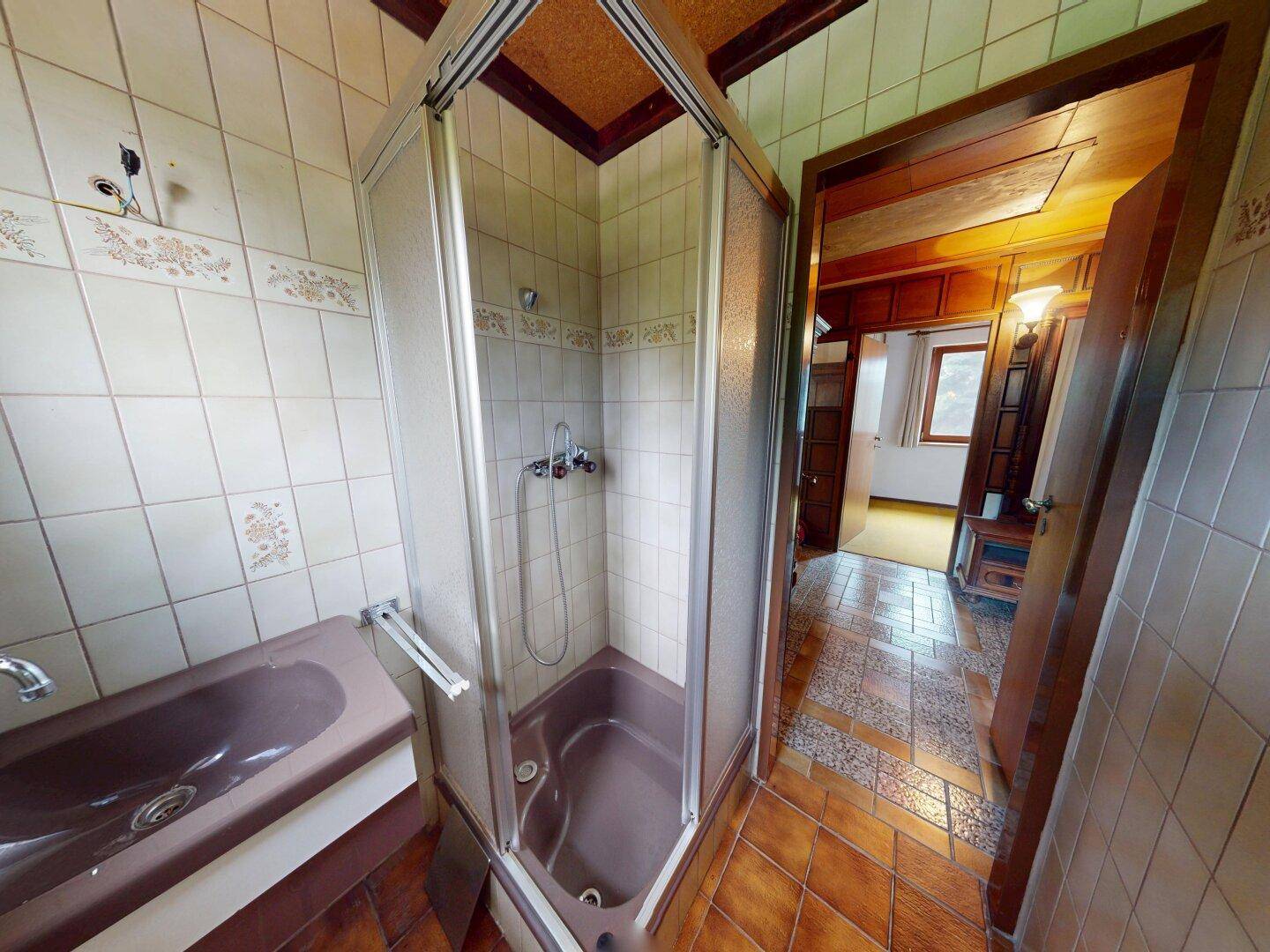 Badezimmer mit Duschkabine, braunem Waschbecken und gefliesten Wänden im 80er-Jahre-Stil.
