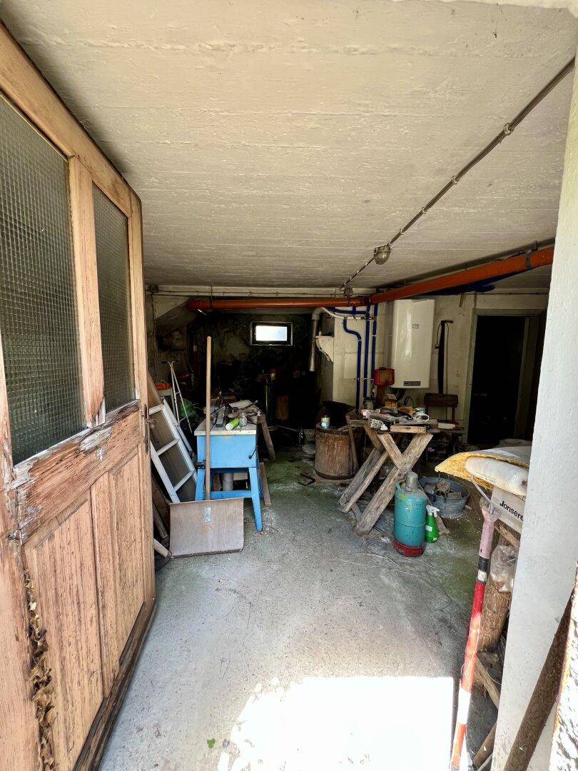 Unaufgeräumter Kellerraum mit Betonboden, sichtbaren Rohren und verschiedenen Werkzeugen.