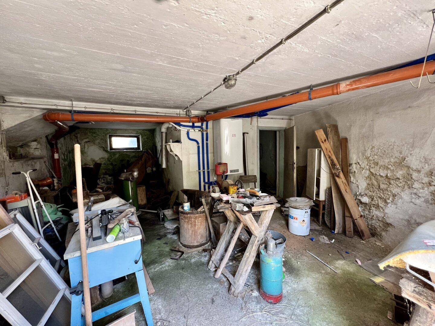 Geräumiger Kellerraum mit Betonboden, sichtbaren Rohren und Lagergegenständen.