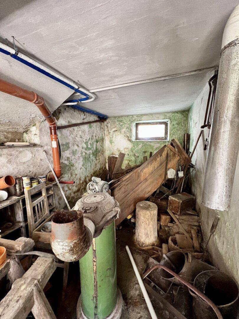 Kellerraum mit feuchten Wänden, kleinem Fenster und gelagerten alten Gegenständen.