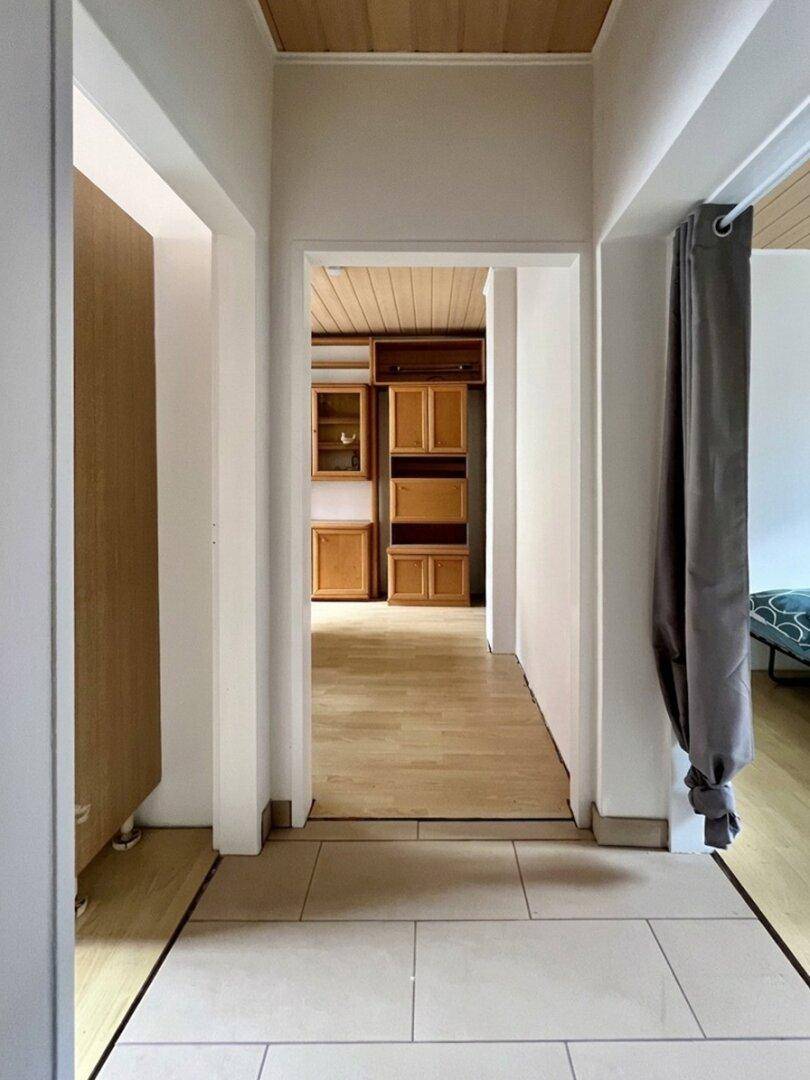 Heller Flur mit Holzdecke und Fliesenboden, der zu einem Raum mit Holzschränken führt.