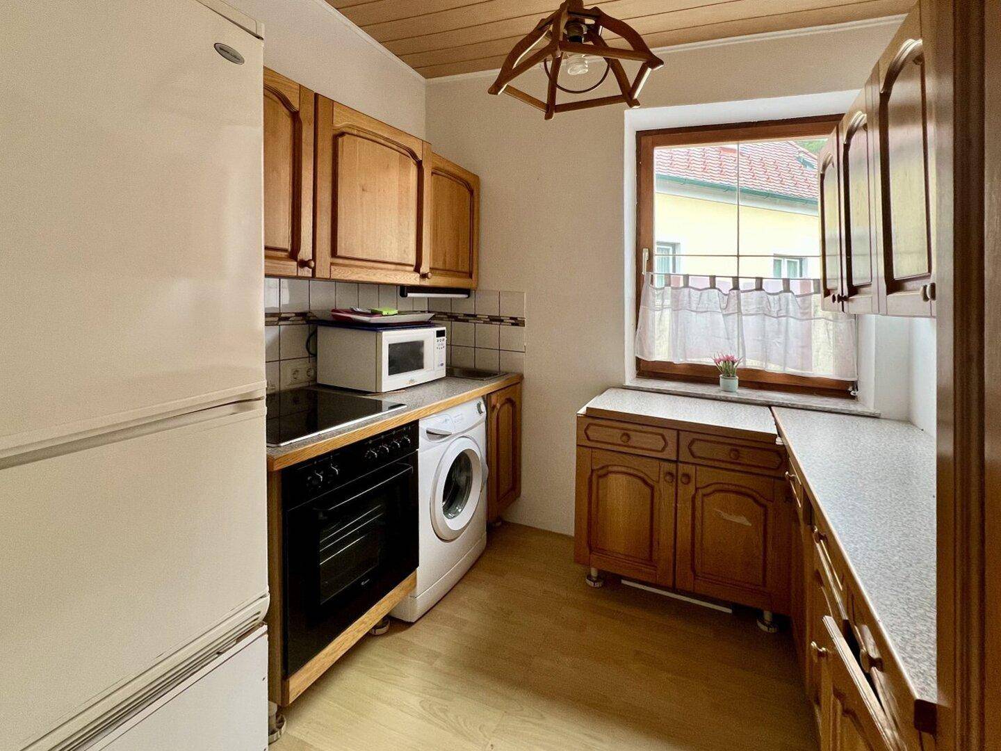 Traditionelle Küche mit Holzschränken, Fenster und älteren Geräten, inklusive Waschmaschine.