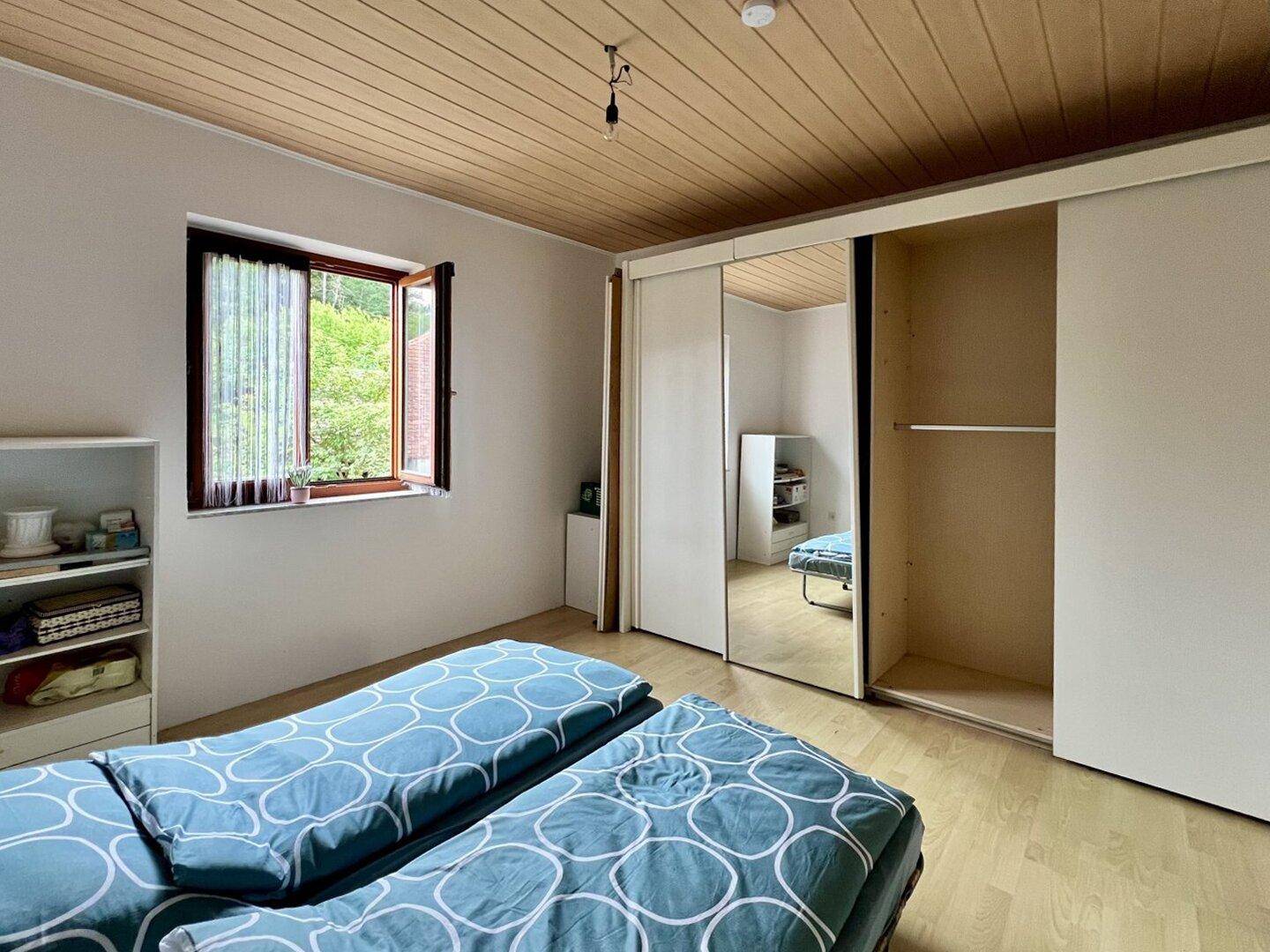Schlafzimmer mit Holzdecke, zwei Einzelbetten und einem Spiegelschrank.