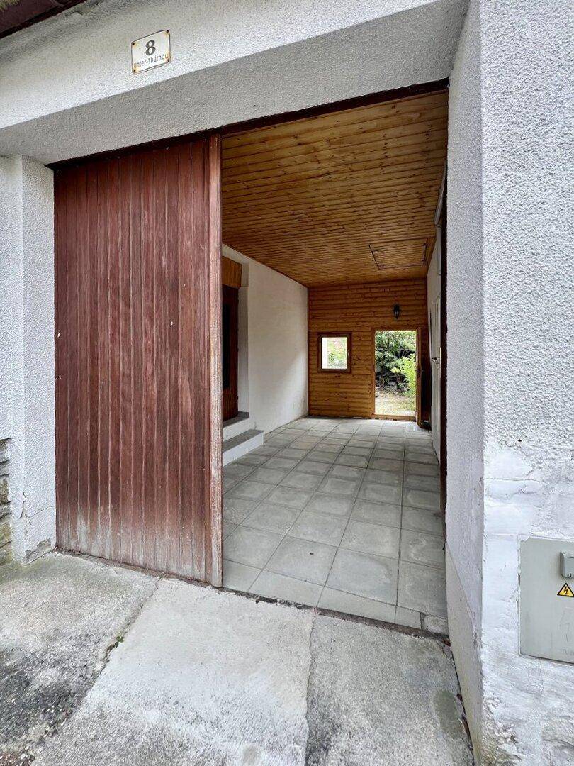 Überdachter Eingangsbereich mit Fliesenboden und Holzdecke, führt zum Haus.