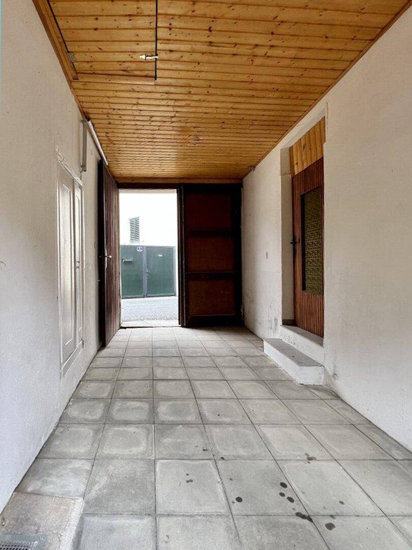 Langer überdachter Gang mit Fliesenboden und Holzdecke, führt zu einem weiteren Eingang.