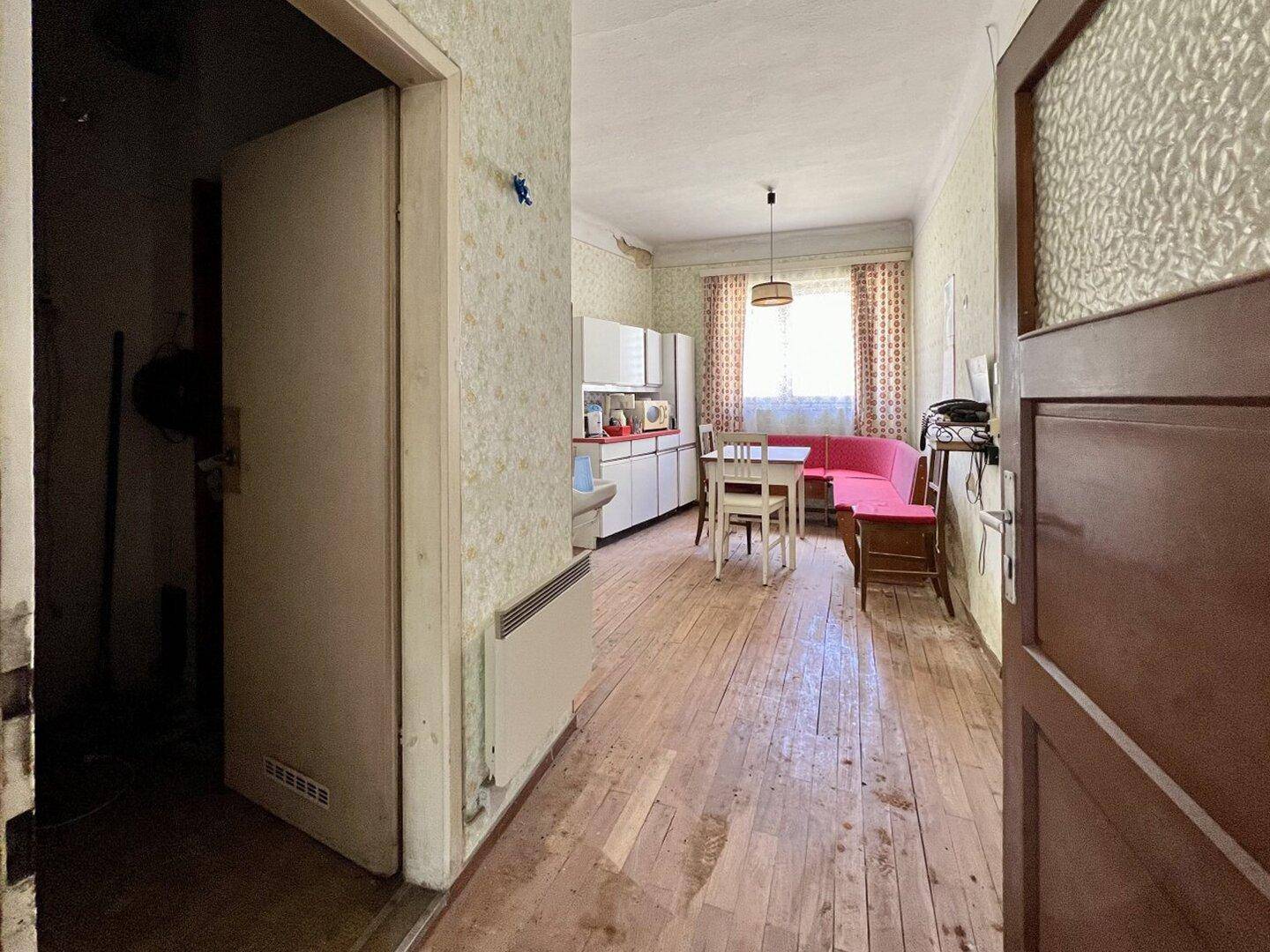 Einfache Wohnküche mit Esstisch, älteren Möbeln und gemusterter Tapete.