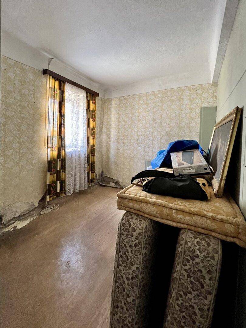 Renovierungsbedürftiger Raum mit abblätternder Tapete, altem Boden und Fenster.