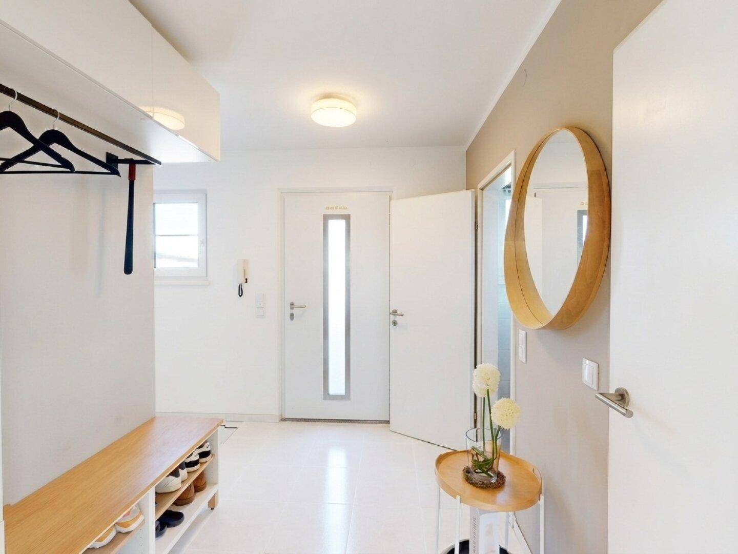 Heller Eingangsbereich mit Garderobe, Schuhregal und einem runden Spiegel an der Wand.