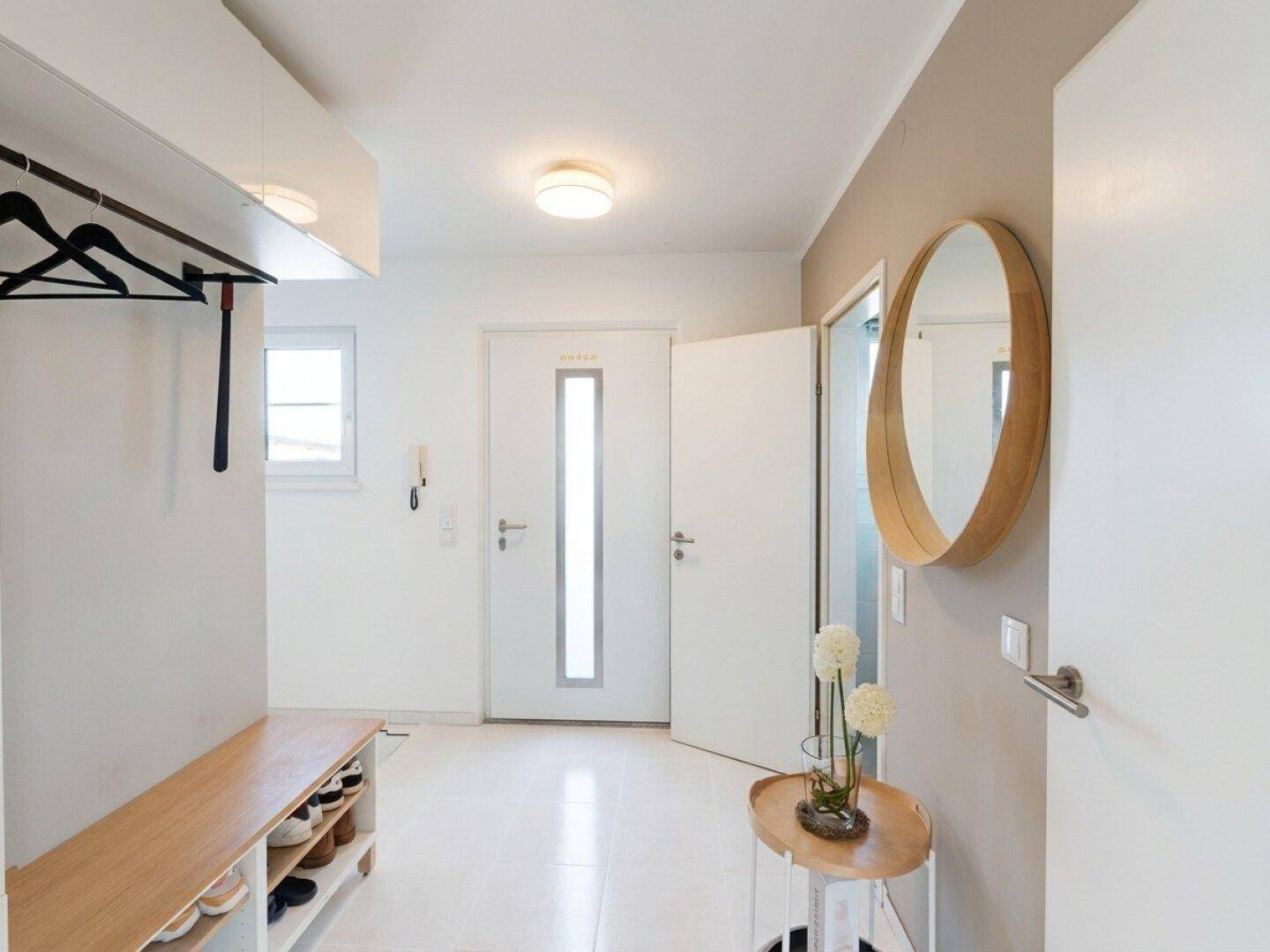 Heller Eingangsbereich mit Garderobe, Schuhbank und einem runden Spiegel an der Wand.