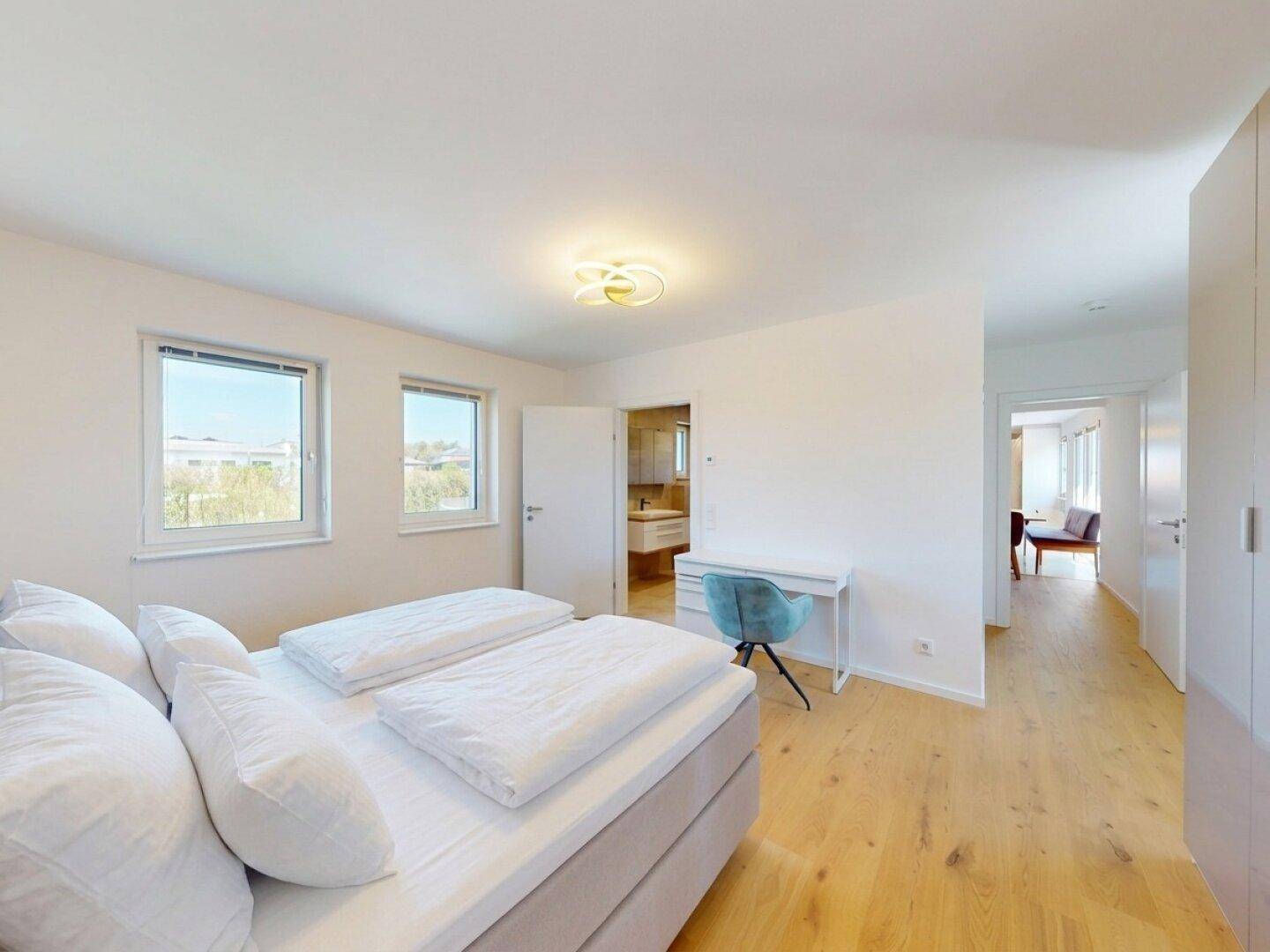 Helles Schlafzimmer mit Doppelbett, Holzboden und Zugang zu einem angrenzenden Badezimmer.