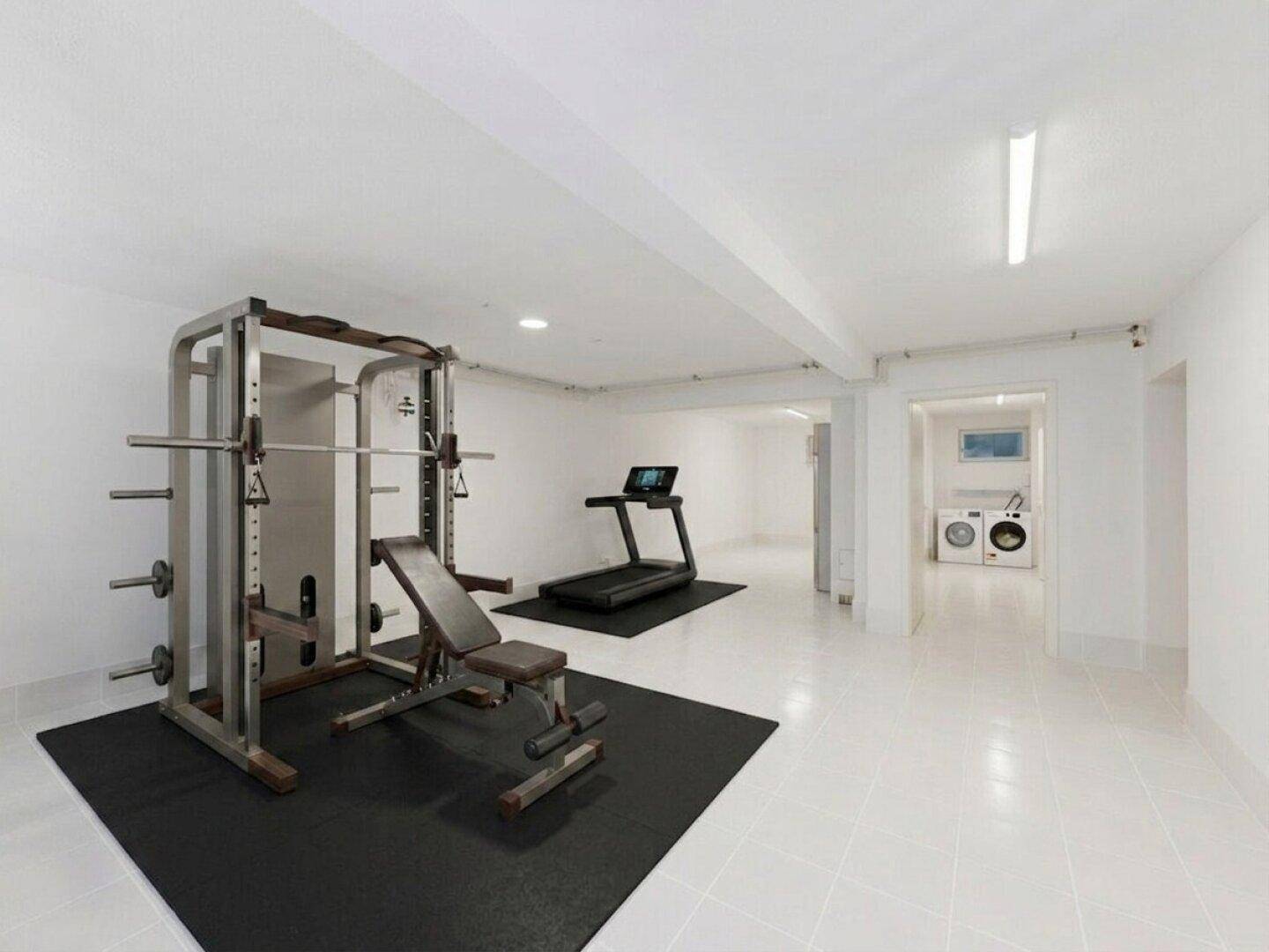 Geräumiger Fitnessraum im Keller mit Trainingsgeräten und angrenzendem Waschraum.