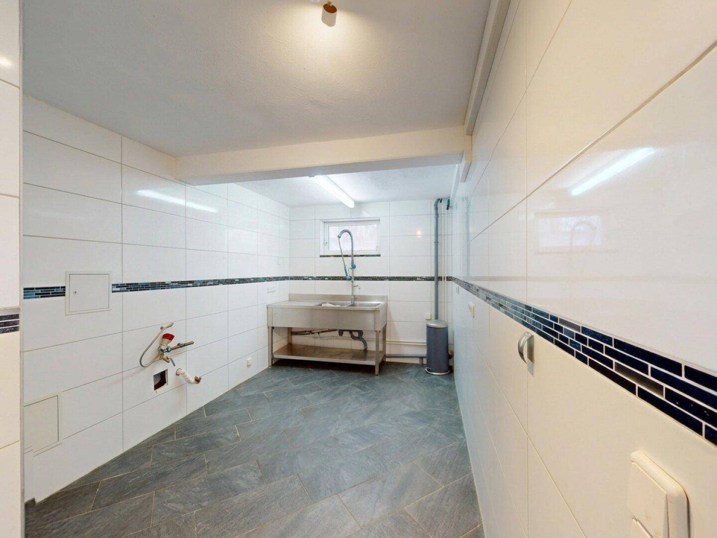 Gefliester Hauswirtschaftsraum im Keller mit Waschbecken und viel Stauraum.