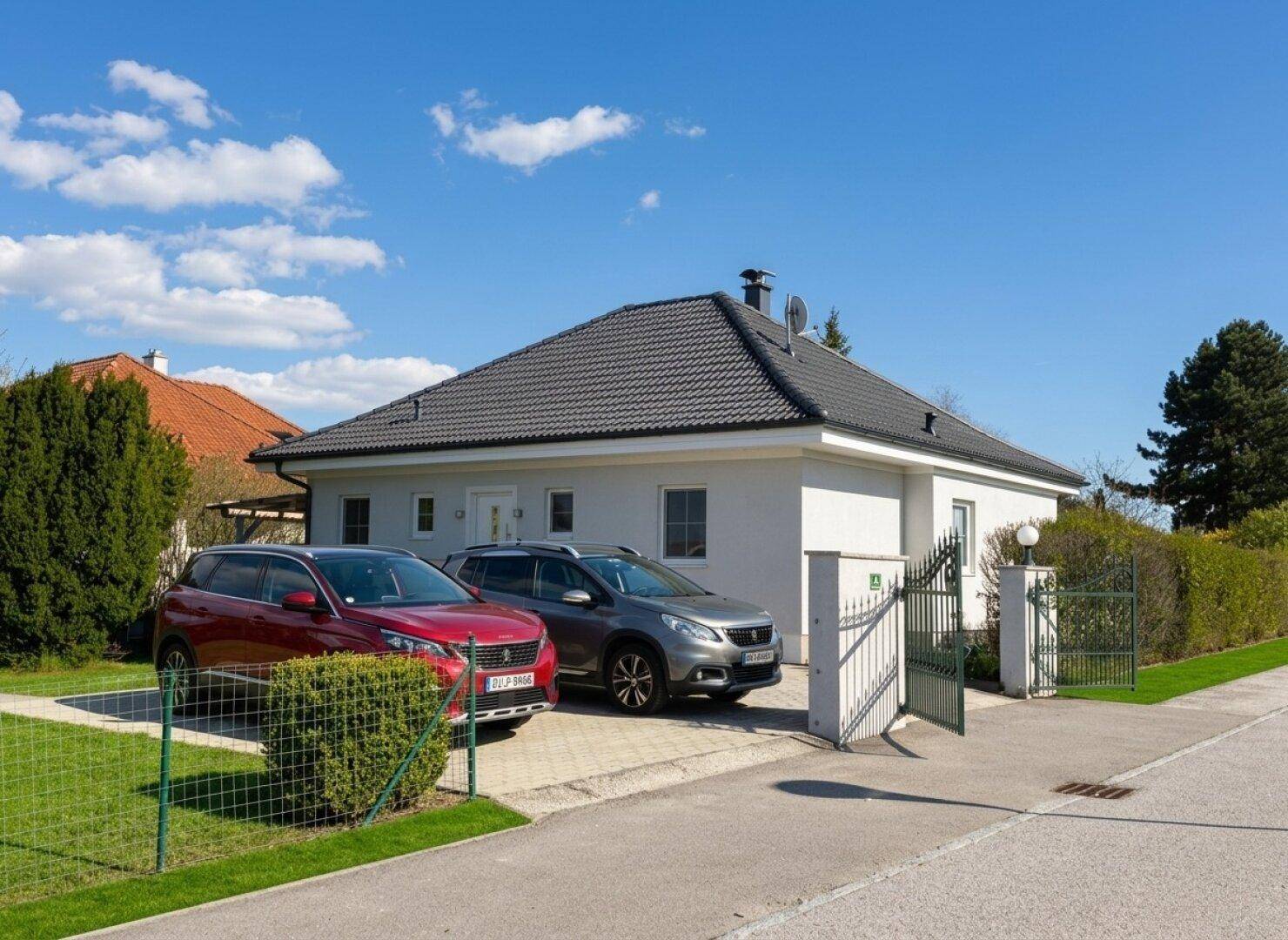 Einfamilienhaus mit gepflegter Auffahrt, zwei Autos und einem grünen Gartentor.