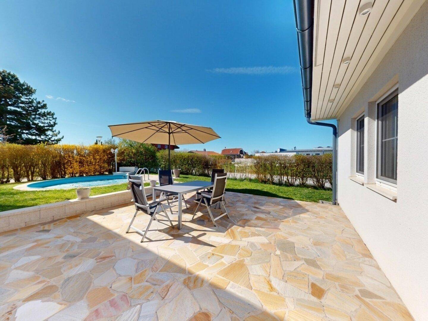 Geräumige Terrasse mit Steinplatten, Gartenmöbeln und Blick auf den Pool und die Hecke.