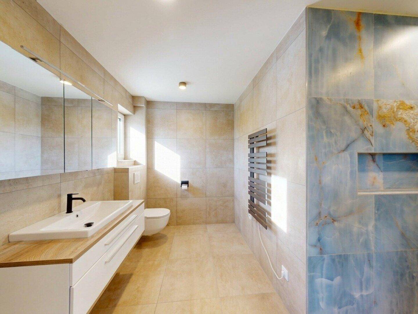 Modernes Badezimmer mit großformatigen Fliesen, wandhängendem WC und Waschtisch mit Holzplatte.
