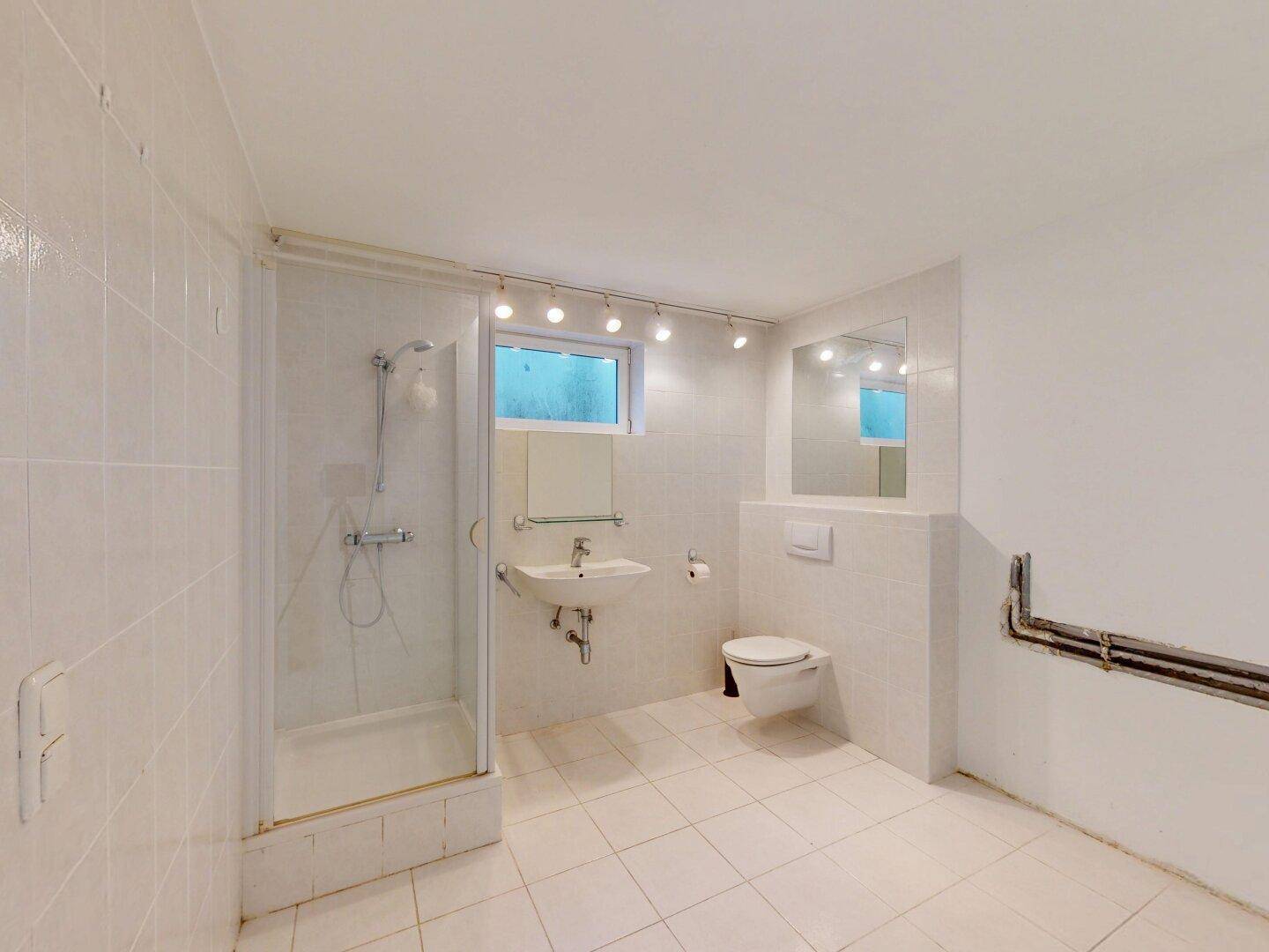 Einfaches Badezimmer im Untergeschoss mit Dusche, WC und Waschbecken.