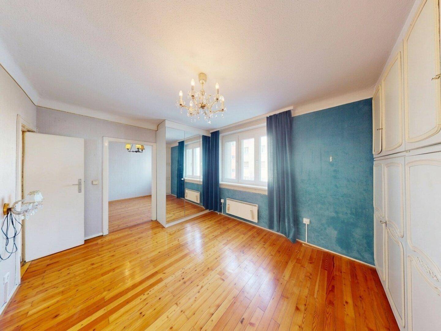 Schlafzimmer mit Holzboden, blauer Akzentwand und Spiegelschränken.