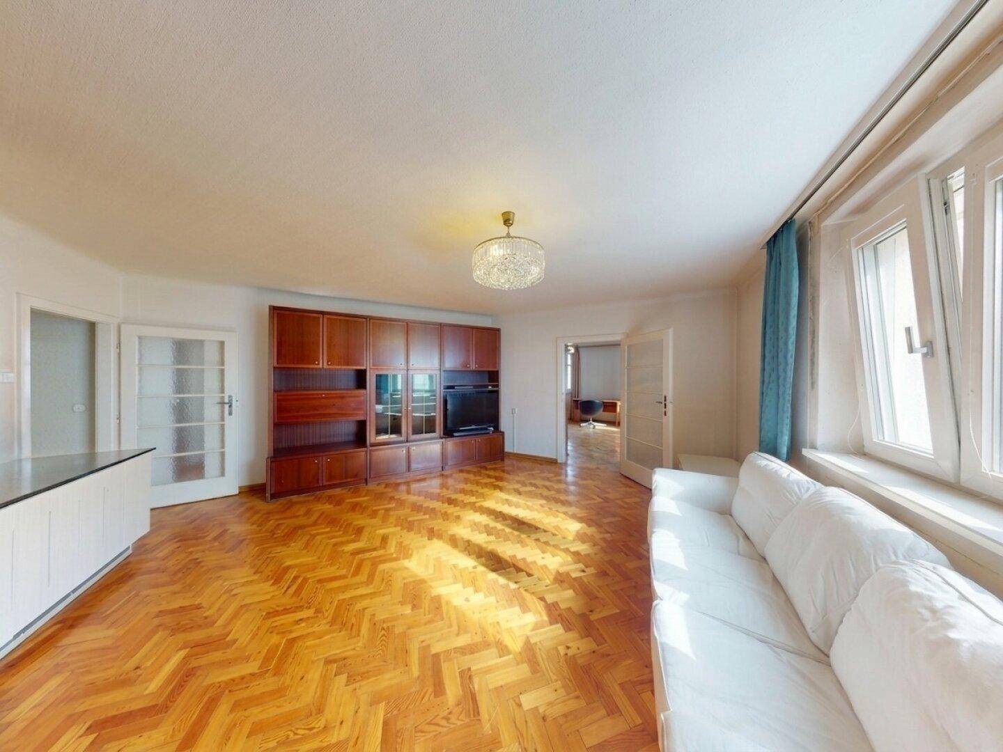 Wohnzimmer mit Fischgrätparkett, Holzschrankwand und weißem Sofa.