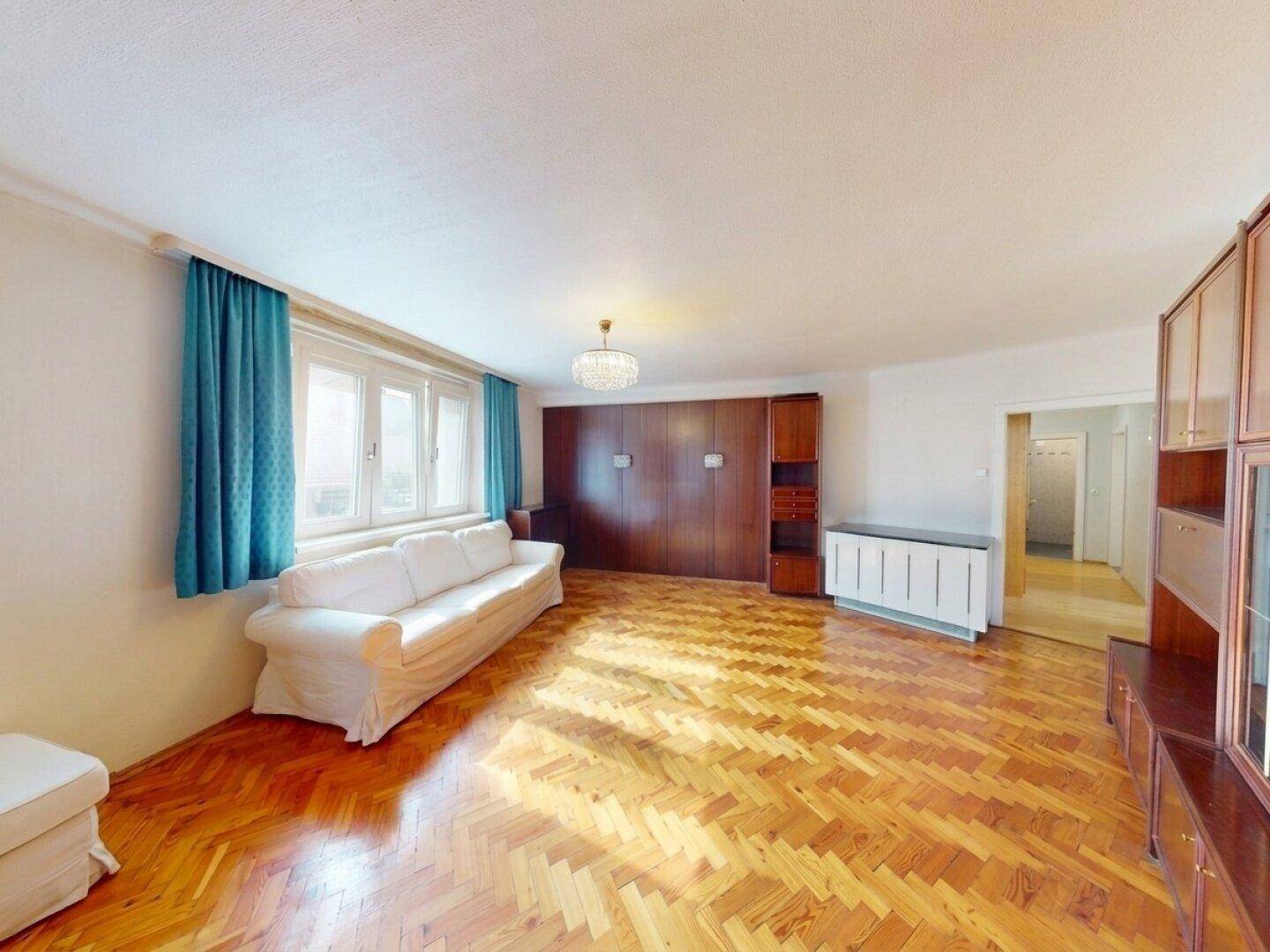 Helles Wohnzimmer mit Fischgrätparkett, Holzschrankwand und blauen Vorhängen.