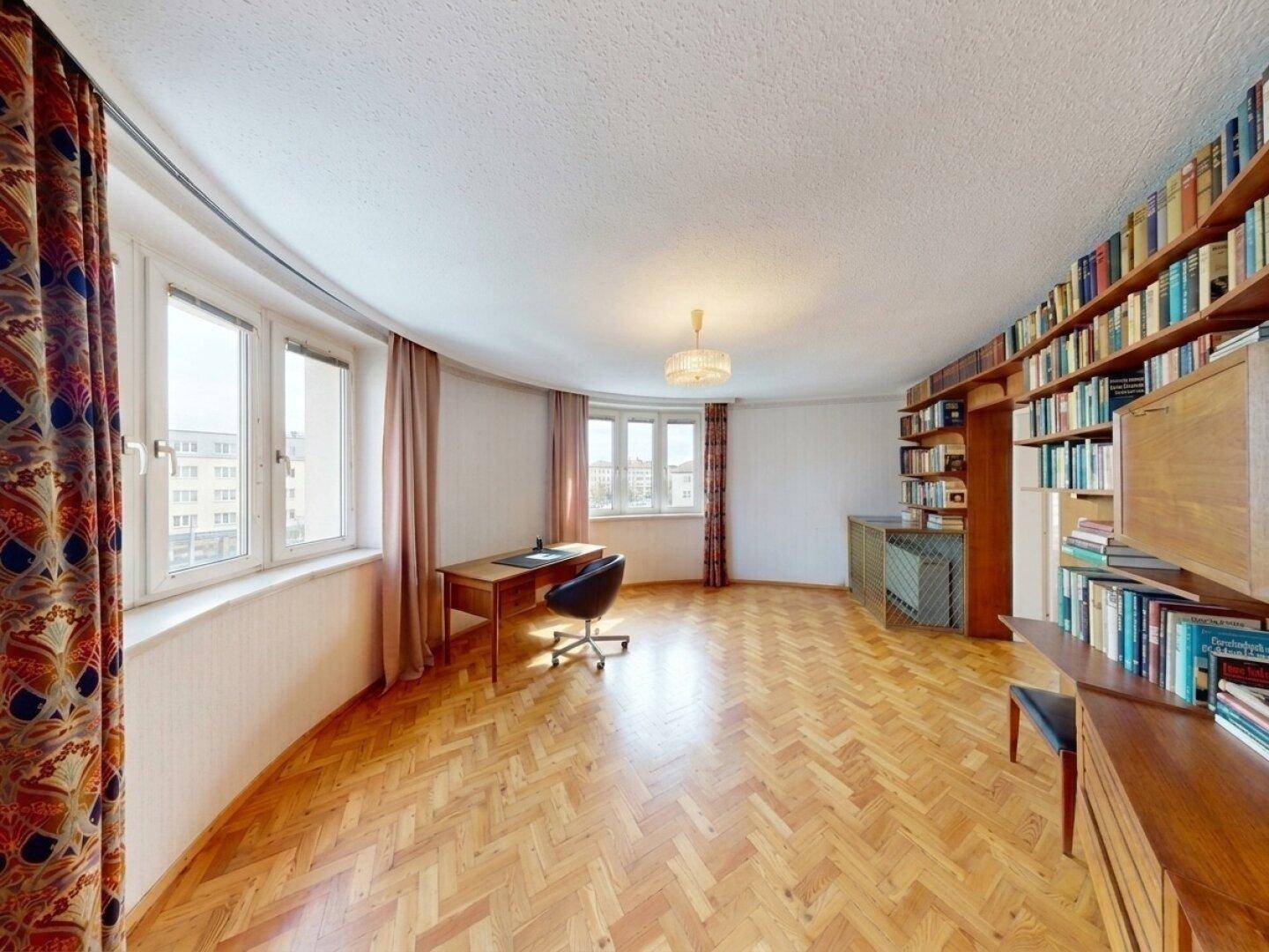 Geräumiges Arbeitszimmer mit Bücherregalen, Schreibtisch und Fischgrätparkett.