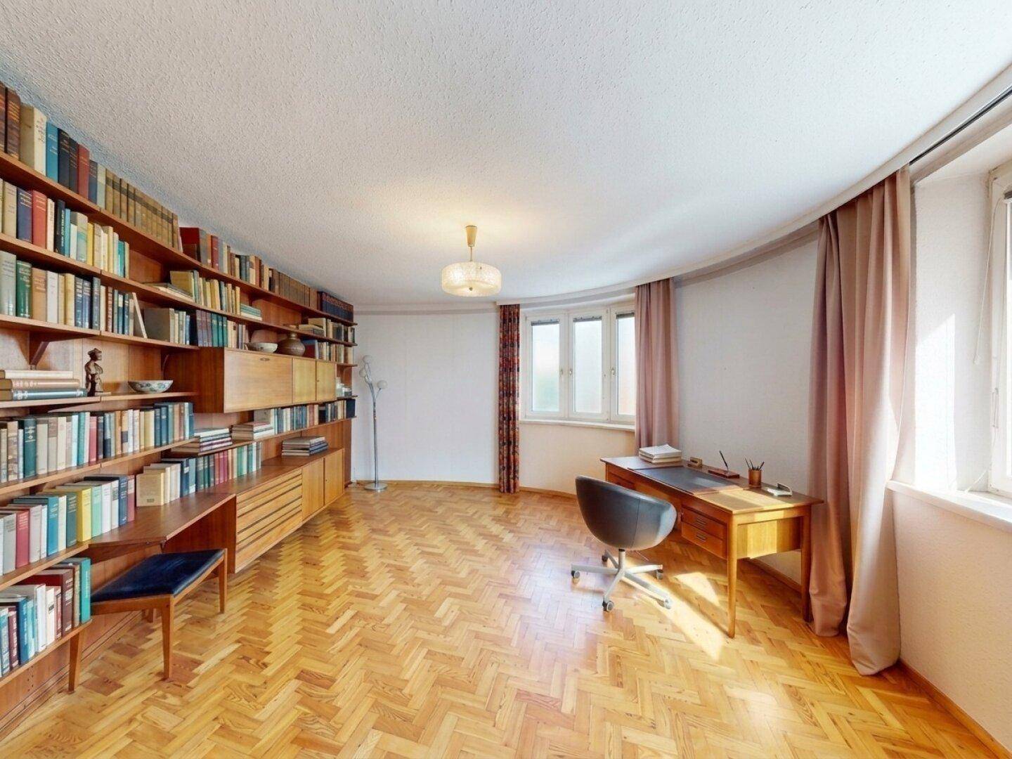 Arbeitszimmer mit umfangreicher Bücherwand, Schreibtisch und hellem Fischgrätparkett.