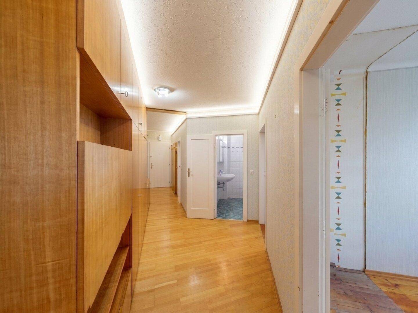Langer Flur mit Holzvertäfelung, Einbauschränken und Zugang zum Badezimmer.