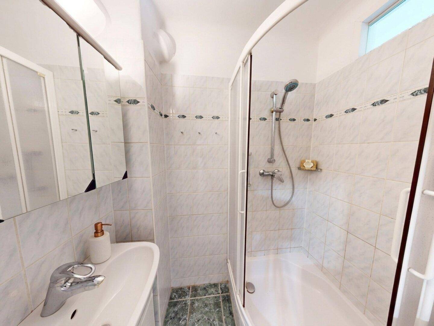 Badezimmer mit Duschkabine, Waschbecken und weißen Fliesen.
