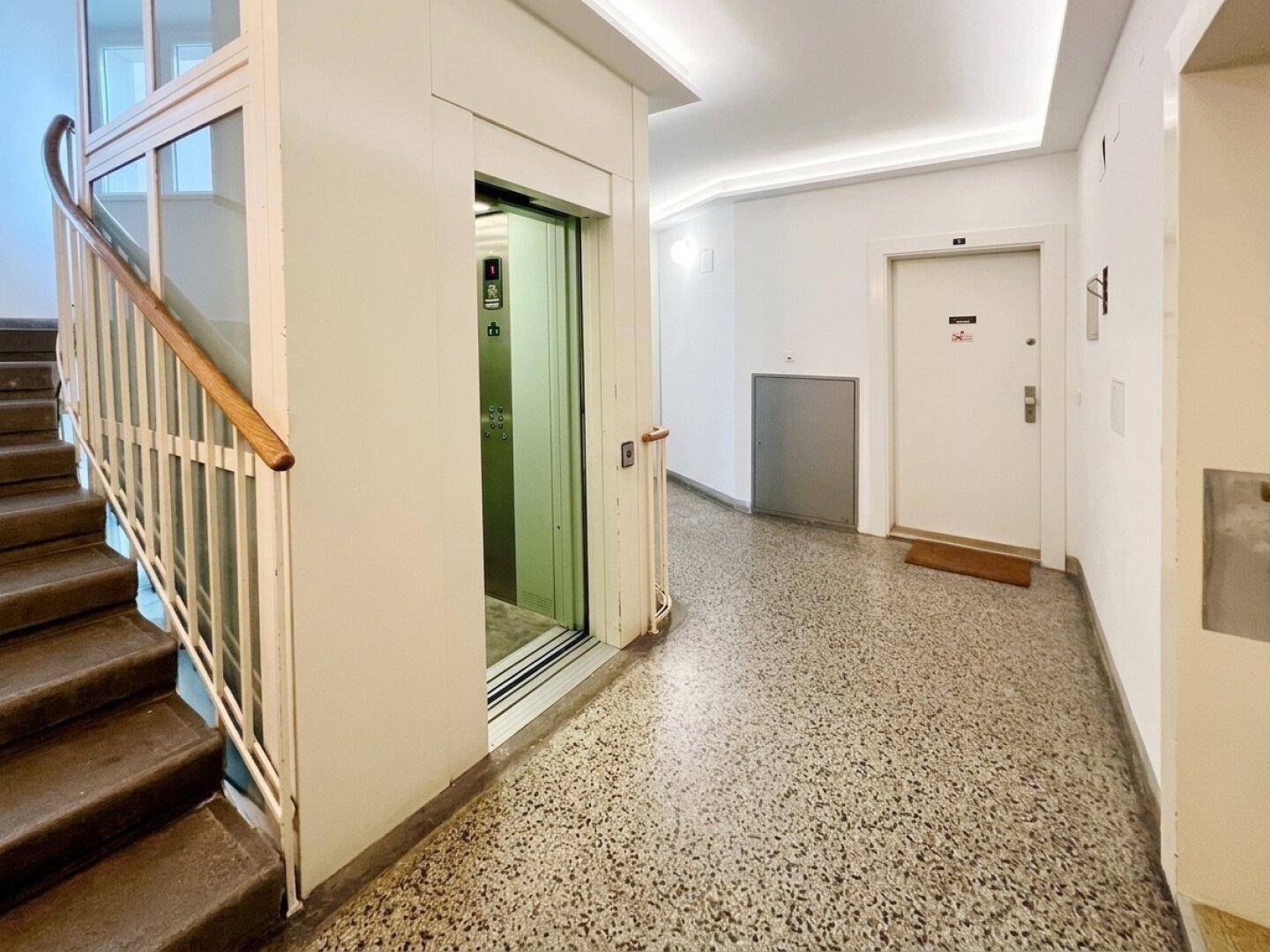 Eingangsbereich mit Treppenhaus, Aufzug und Terrazzoboden.