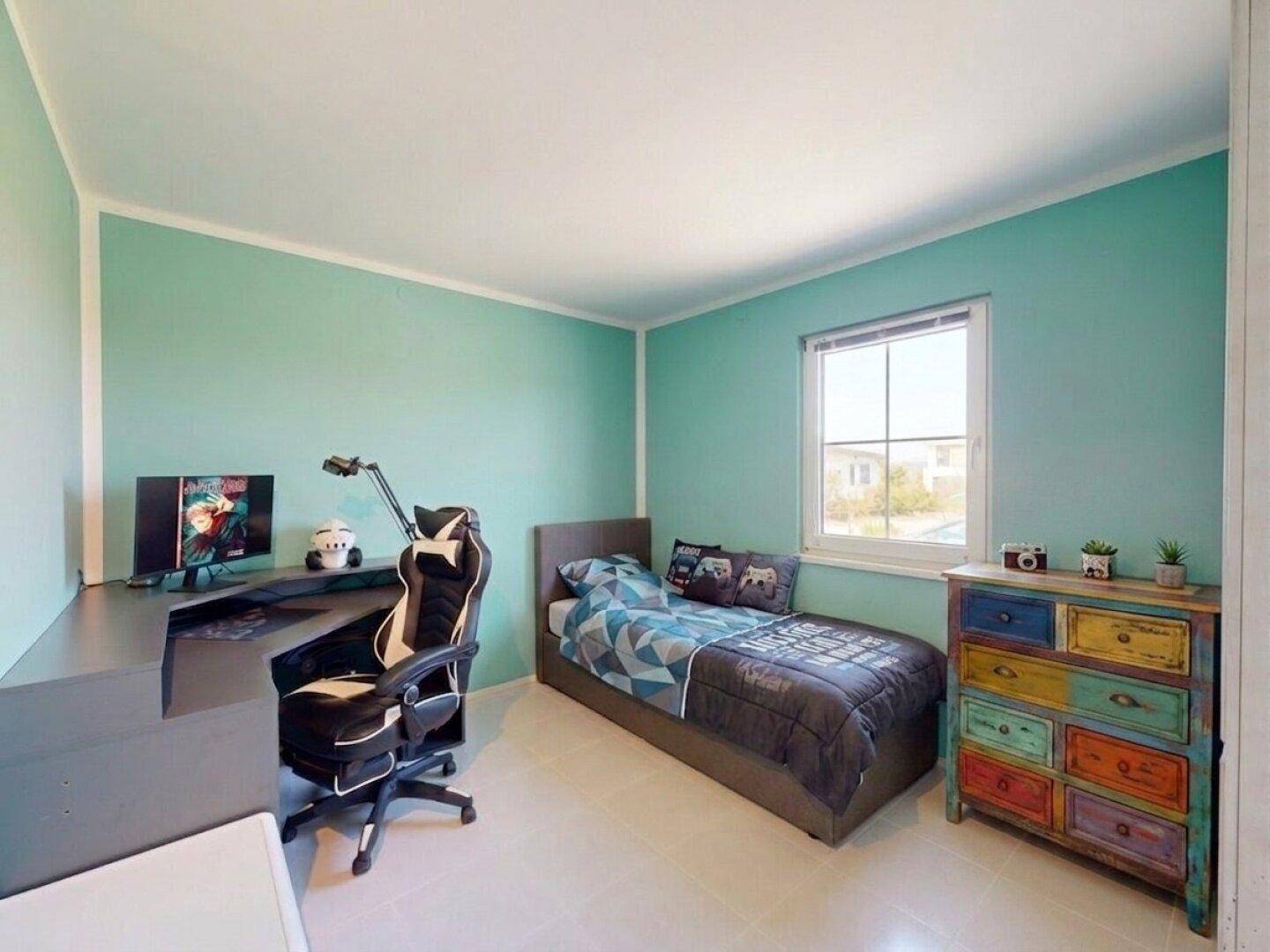 Kinderzimmer mit hellem Bett, Schreibtisch und bunter Kommode in frischen Farben.