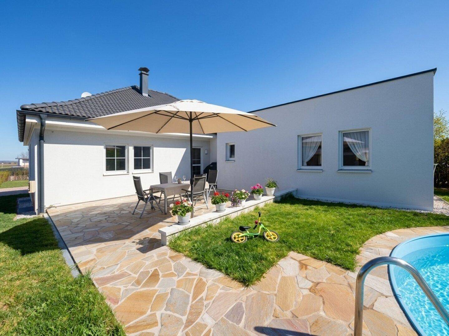 Gepflegter Gartenbereich mit Steinterrasse, Rasenfläche und kleinem Swimmingpool.