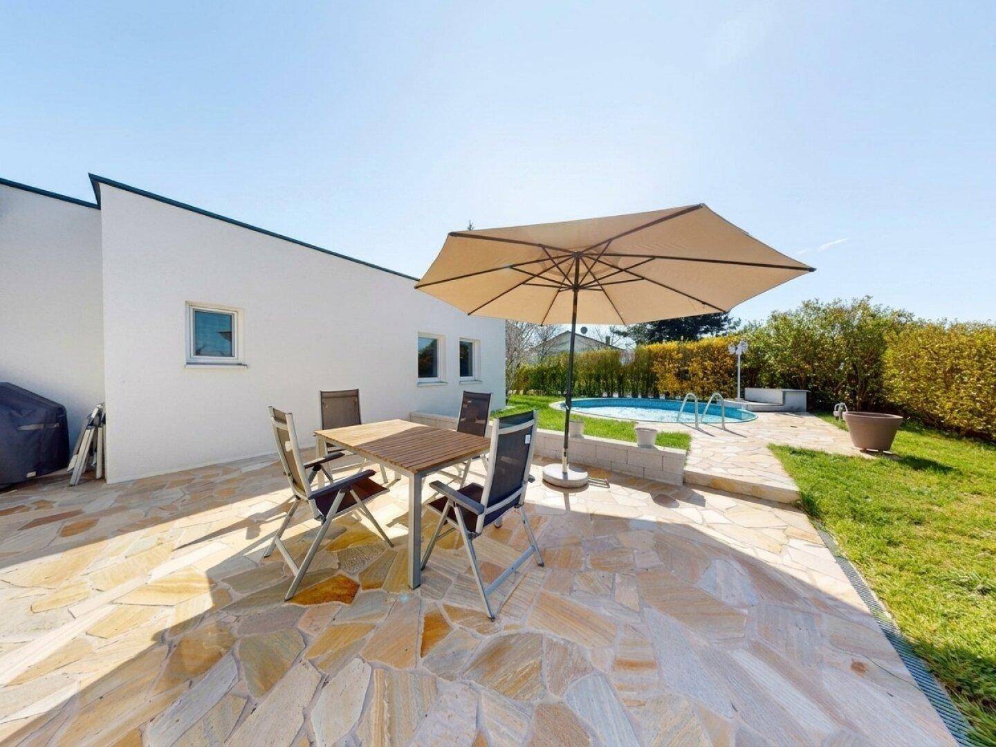 Großzügige Steinterrasse mit Gartenmöbeln und Sonnenschirm, angrenzend an den Pool.