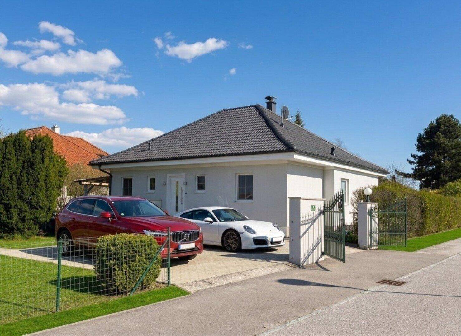 Gepflegtes Einfamilienhaus mit zwei Autos in der Auffahrt unter strahlend blauem Himmel.
