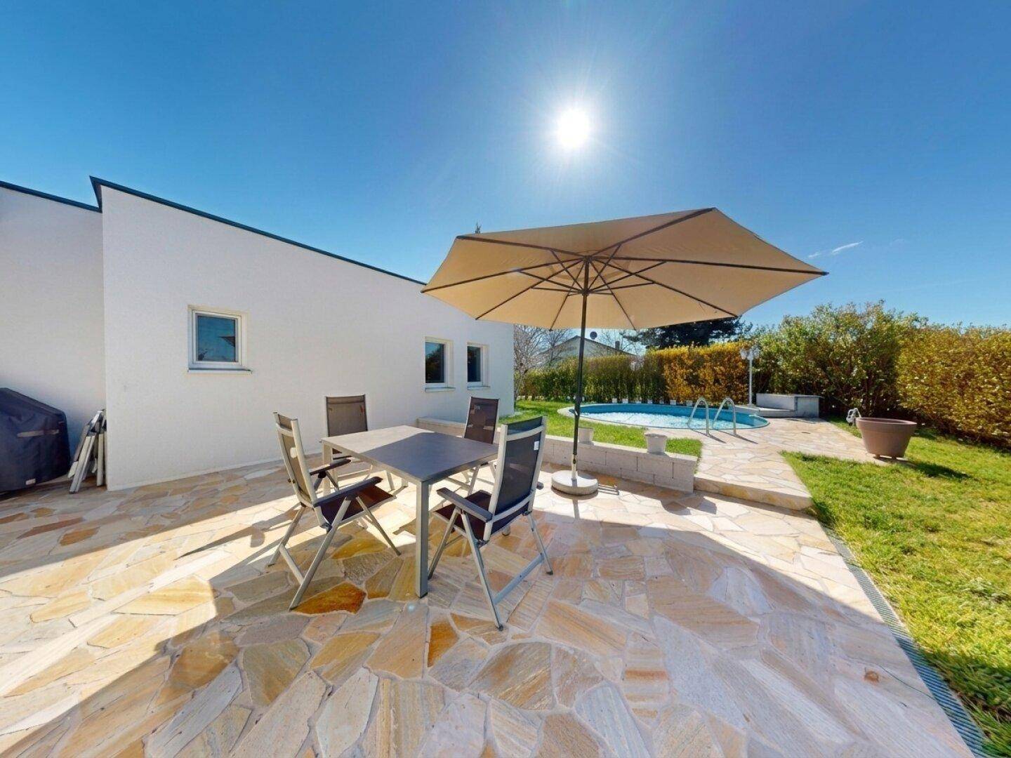 Geräumige Steinterrasse mit Sonnenschirm und Gartenmöbeln, angrenzend an den Poolbereich.