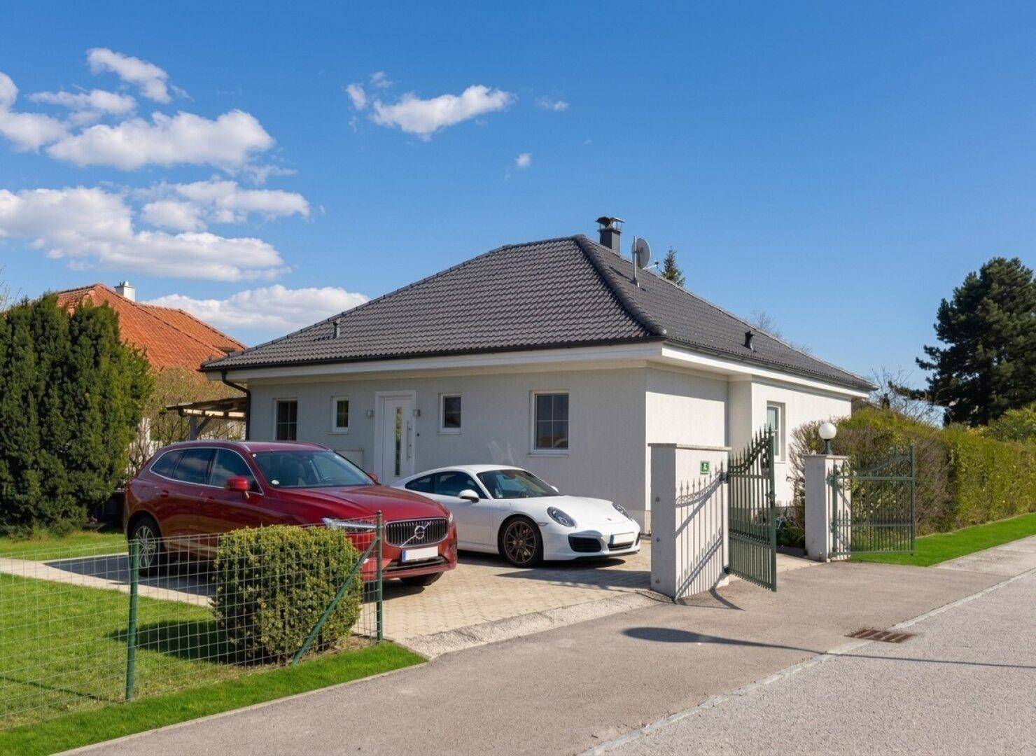 Einfamilienhaus mit gepflegter Auffahrt und zwei Fahrzeugen unter blauem Himmel an einem sonnigen Tag.