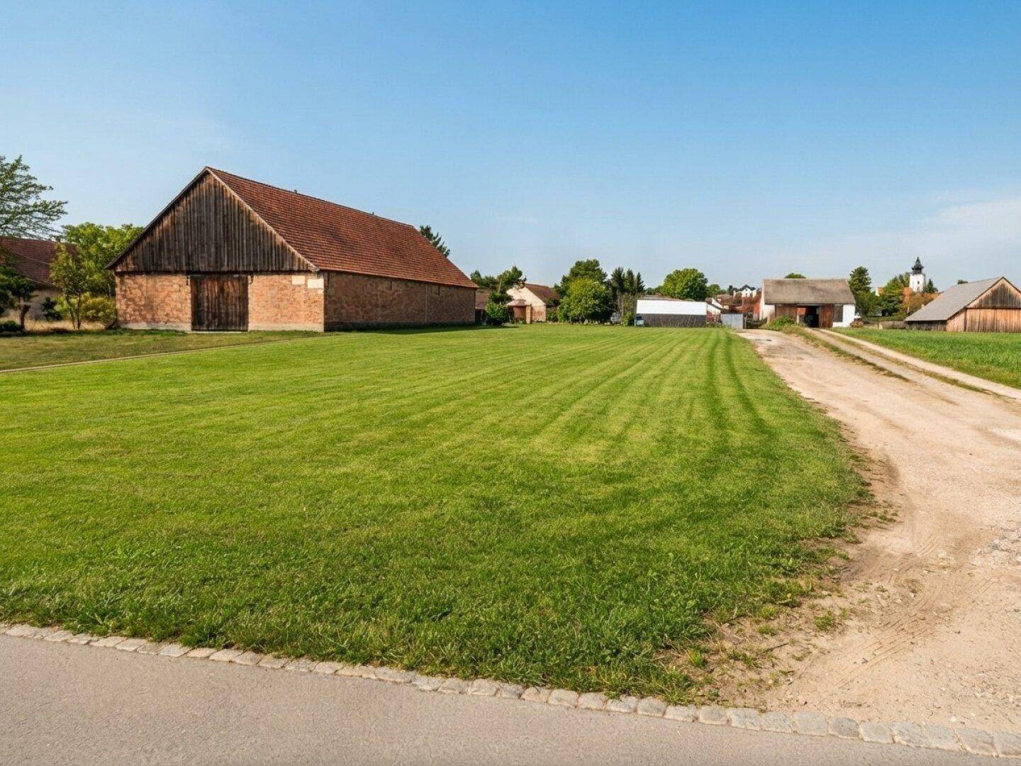 Weitläufiges grünes Grundstück mit ländlicher Umgebung und alter Scheune im Hintergrund.