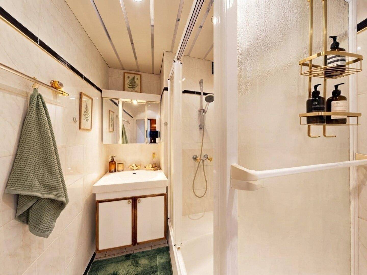Kleines Badezimmer mit Duschkabine, Waschbecken und hellen Fliesen im 80er-Jahre-Stil.