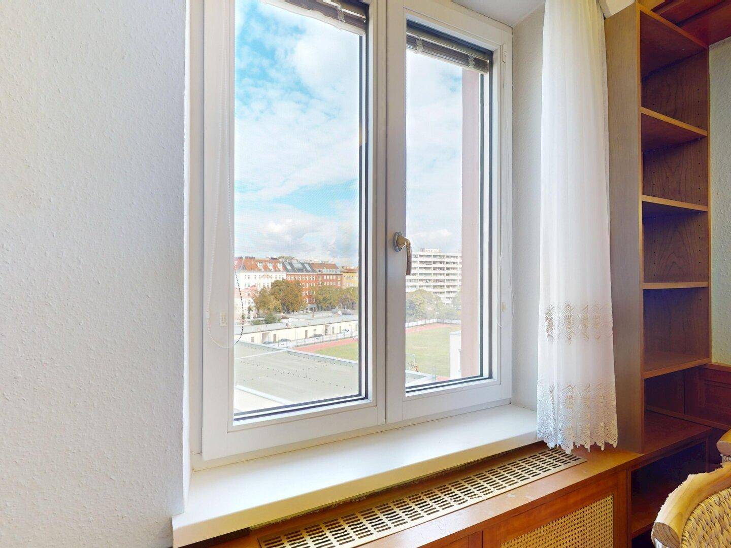 Fenster mit weitem Blick über die Stadt und einen Sportplatz, das viel Tageslicht hereinlässt.