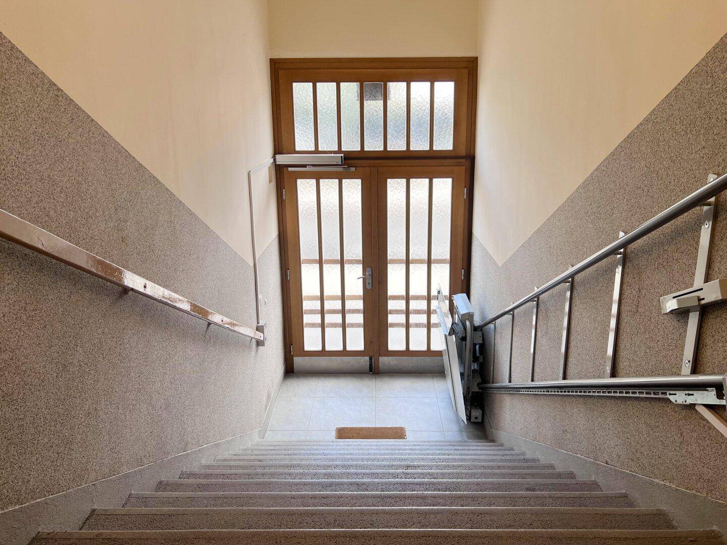 Treppenhaus mit Treppenlift für Barrierefreiheit und einer Holztür am oberen Ende.