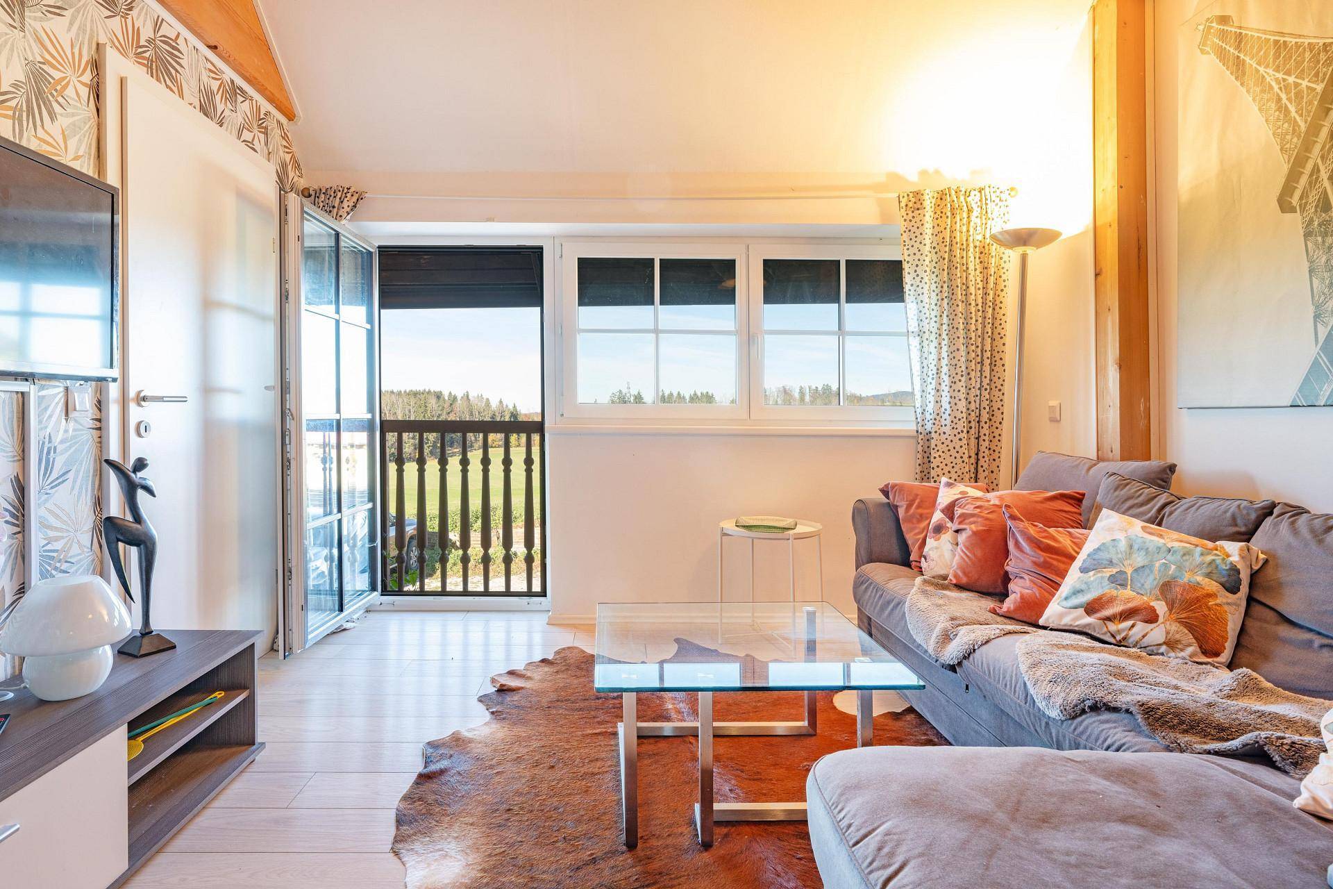 Sonniges Wohnzimmer mit gemütlicher Couch, Holzbalkendecke und Zugang zu einem französischen Balkon.