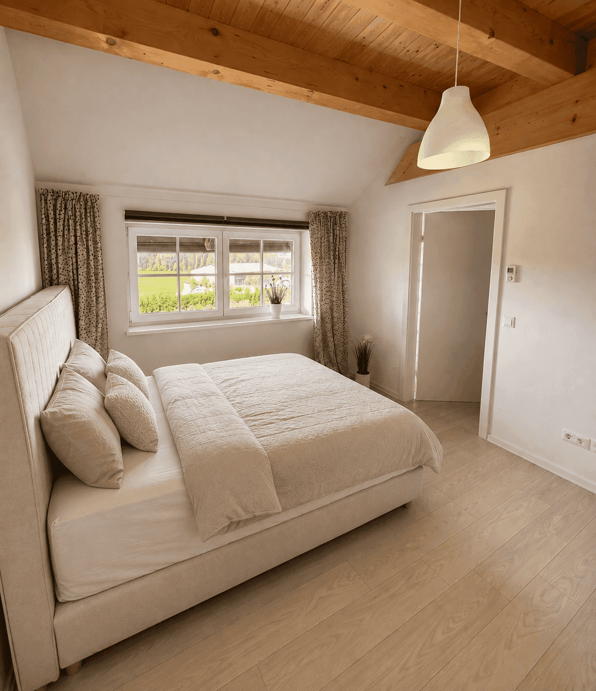 Helles Schlafzimmer mit großem Bett, Holzboden und Blick ins Grüne durch die Fenster.