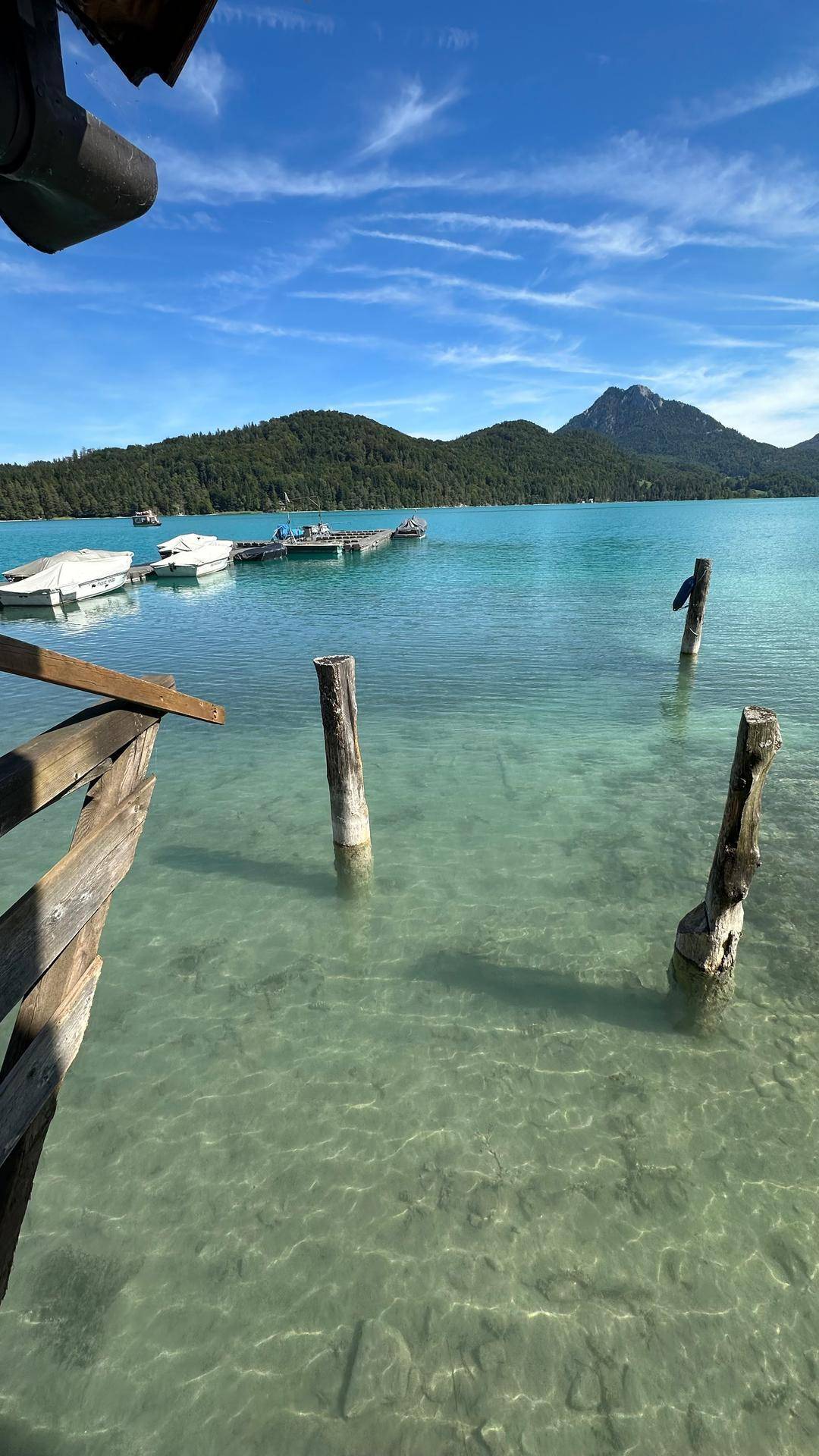 Idyllischer Blick auf einen klaren, türkisfarbenen See mit bewaldeten Bergen unter blauem Himmel.