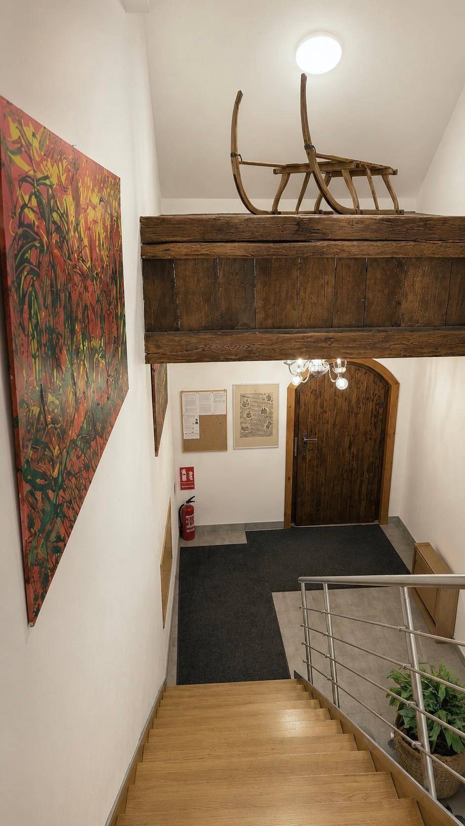 Holztreppe führt nach unten, mit rustikalem Holzbalken und Kunstwerk an der Wand.