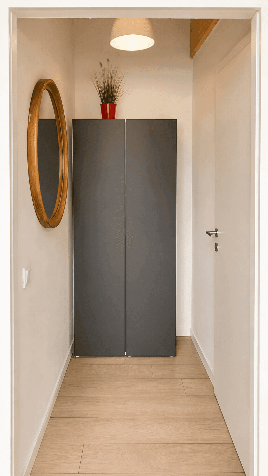 Schmaler Flur mit dunklem Schrank, rundem Spiegel und hellem Holzboden.